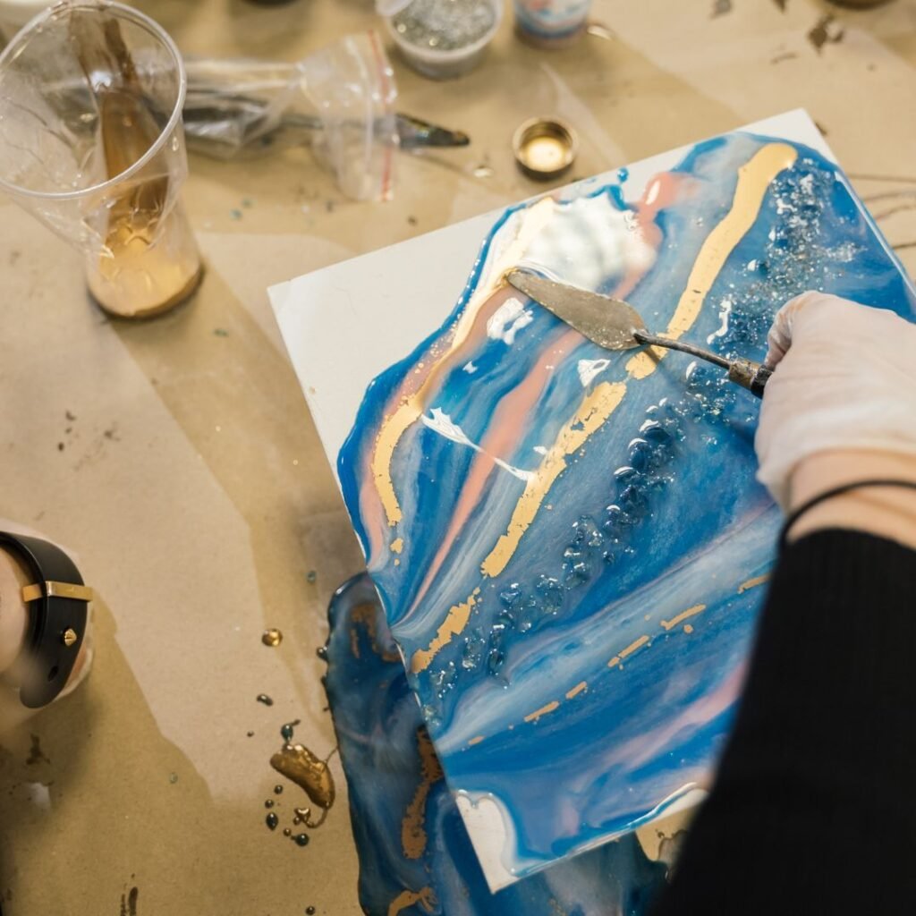A person mixing resin in a cup with a blue colored liquid in a resin art workshop in Qatar